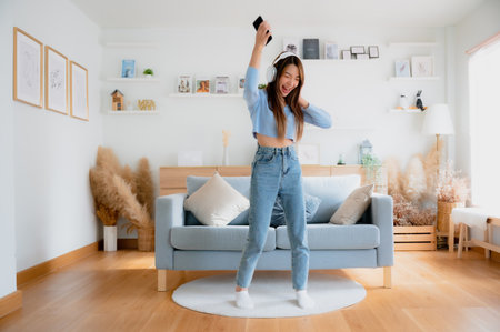 Young asian woman dancing in living room. Asian woman with a smile relaxing at home, happy and in good mental and physical health, wearing headset and listening to musicの写真素材