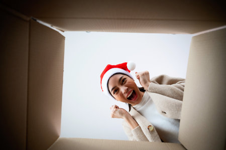 Happy young asian woman wearing christmas hat and unpacking gift box. Beautiful female smiling and surprised while opening present and looking inside. Happy new year, Merry christmas and Thankgiving conceptの写真素材