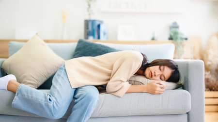 Asian woman resting at home on couch, feeling exhausted after work, lacking energy, or overworked, too tired, and lacking motivationの写真素材