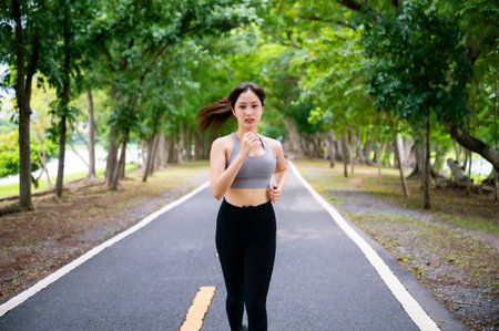 Asian woman running outdoor in public park. Female jogging on the road in morning. Healthy lifestyle concept, sports outdoor activities in parkの写真素材