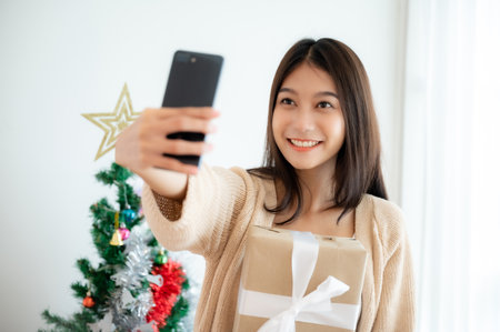 Young asian woman having fun taking selfie and video call talking with her friend. Female showing gift box while on video conversation with friend. Happy new year, Thanksgiving, Merry Christmasの写真素材