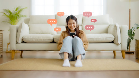 Young asian woman using mobile smartphone in living room. Online live chat chatting on application communication digital media website and social networkの写真素材