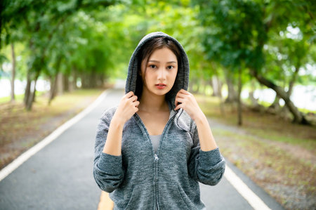 Asian woman wearing jacket is engaged in fitness in public park. Healthy lifestyle concept, sports outdoor activities in parkの写真素材