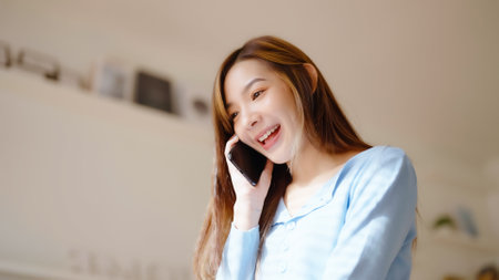 Happy young asian woman speaking on mobile phone at home, Female teen answering call on cellphone while sitting in couch. Asia girl talking on smartphoneの写真素材