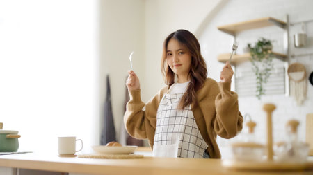 Happy young asian woman wearing apron and standing in kitchen room. Beautiful female smiling and looking at camera feeling confidentの写真素材