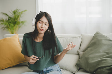 Asian women are listening to music in living room at home. She sitting on sofa and relaxing happy leisure activity at weekendの写真素材