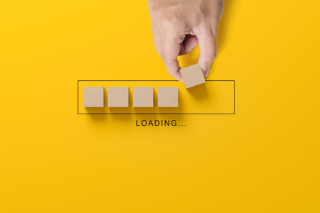 Loading concept. Hand putting wooden block cubes for upload preparation progress on yellow backgroundの写真素材