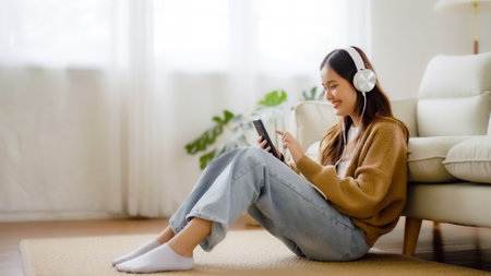 Happy young asian woman relaxing at home. Female smile sitting on sofa and holding mobile smartphone. Girl using video call to friendの写真素材