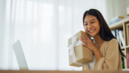 Young asian woman using computer laptop at home. Female showing gift box while on video conversation with friend. Happy birthday, Happy new year, Thanksgivingの写真素材