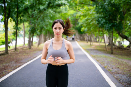 Asian woman running outdoor in public park. Female jogging on the road in morning. Healthy lifestyle concept, sports outdoor activities in parkの写真素材