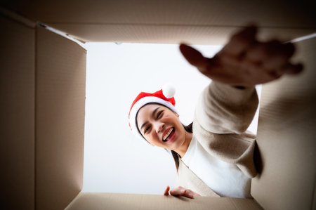 Happy young asian woman wearing christmas hat and unpacking gift box. Beautiful female smiling and surprised while opening present and looking inside. Happy new year, Merry christmas and Thankgiving conceptの写真素材