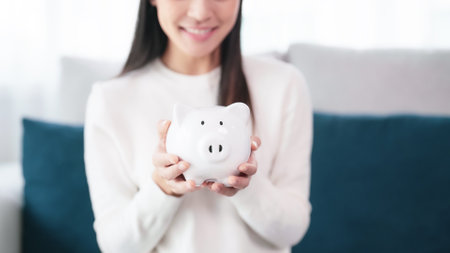 Young asian woman holding white piggy bank at home. Save money and investment conceptの写真素材