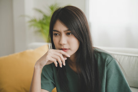 Upset asian woman frustrated by problem with work or relationships, sitting on couch, feeling despair and anxiety, loneliness, having psychological troubleの写真素材