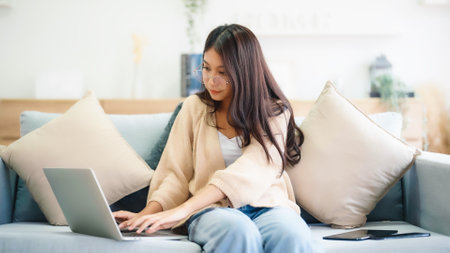 Young asian woman using laptop while seated on couch at homeの写真素材