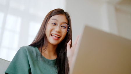 Smiling young asian woman working on laptop at home. Attractive asia female using computer remote studying, watching online education and video callingの写真素材