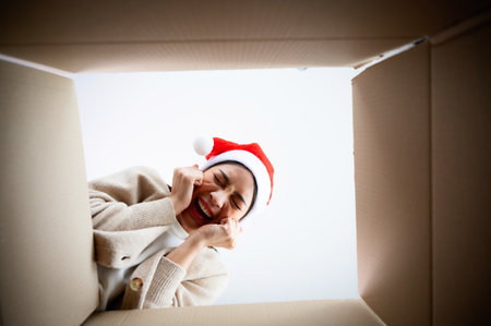 Happy young asian woman wearing christmas hat and unpacking gift box. Beautiful female smiling and surprised while opening present and looking inside. Happy new year, Merry christmas and Thankgiving conceptの写真素材