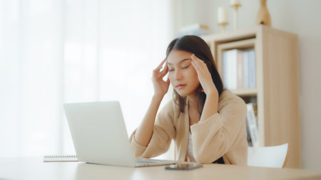 Office syndrome. Overworked tired young asian woman feeling headache, having eyesight problem after computer laptop work. Stressed young woman suffering from fatigue at homeの写真素材