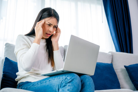 Office syndrome. Overworked tired young asian woman feeling headache, having eyesight problem after computer laptop work. Stressed young woman suffering from fatigue at homeの写真素材