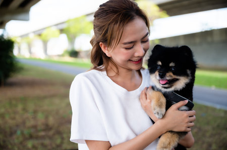 Happy young asian woman playing and holding puppy pomeranian dog black color in the park. Pet lover conceptの写真素材