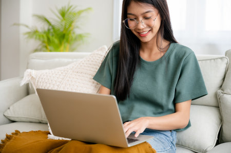 Smiling young asian woman working on laptop at home. Attractive asia female using computer remote studying, watching online education and video callingの写真素材