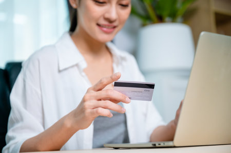Young asian woman working at workplace, makes online banking payments through the internet from bank card on computer laptop. Shopping online on notebook with credit cardの写真素材