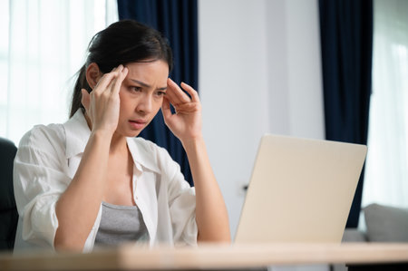 Office syndrome. Overworked tired young asian woman feeling headache, having eyesight problem after computer laptop work. Stressed young woman suffering from fatigue at homeの写真素材