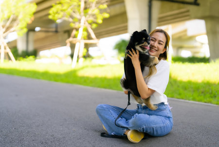 Happy young asian woman playing and sitting on road in the park with her dog. Pet lover conceptの写真素材
