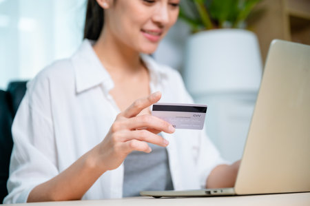 Young asian woman working at workplace, makes online banking payments through the internet from bank card on computer laptop. Shopping online on notebook with credit cardの写真素材