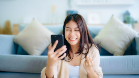 Happy young asian woman relax on comfortable couch at home texting messaging on smartphone, smiling girl use cellphone, chatting online message, shopping online from homeの写真素材