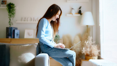Young asian woman using laptop while seated on couch at homeの写真素材