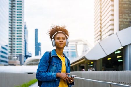 Cheerful black student girl wearing headset and using mobile smartphone, Walking at college building outdoor, Happy and smiling woman teenager. Modern educationの写真素材