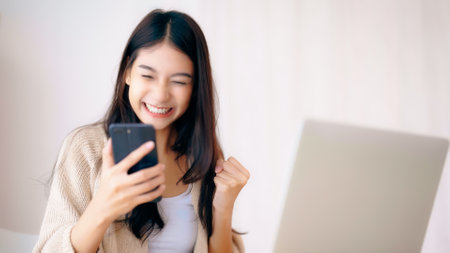 Young asian woman happy working on computer laptop and hand typing chat message on mobile smartphone at home. Video call, Online meetingの写真素材
