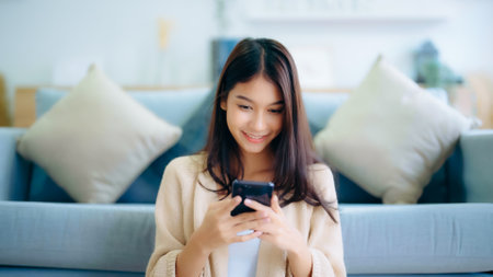 Happy young asian woman relax on comfortable couch at home texting messaging on smartphone, smiling girl use cellphone, chatting online message, shopping online from homeの写真素材