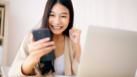 Young asian woman happy working on computer laptop and hand typing chat message on mobile smartphone at home. Video call, Online meetingの写真素材