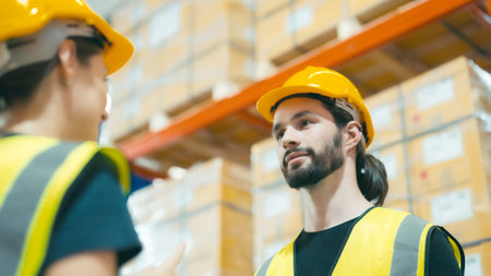 Smiling workers in distribution warehouse having a cheerful conversation. They wearing vest and safety helmet in workの写真素材