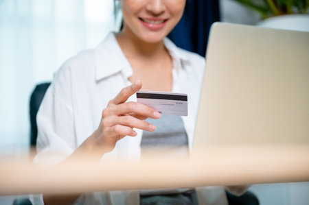 Young asian woman working at workplace, makes online banking payments through the internet from bank card on computer laptop. Shopping online on notebook with credit cardの写真素材