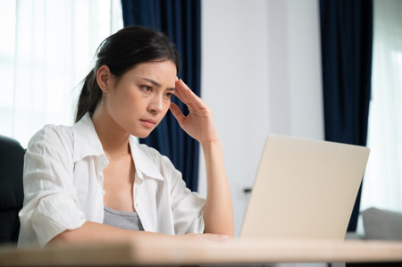 Office syndrome. Overworked tired young asian woman feeling headache, having eyesight problem after computer laptop work. Stressed young woman suffering from fatigue at homeの写真素材