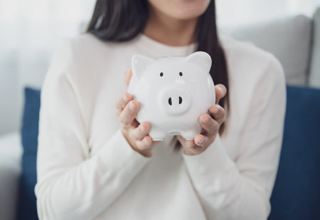 Young asian woman holding white piggy bank at home. Save money and investment conceptの写真素材