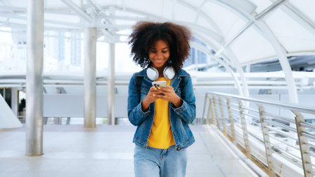 Happy young afro woman listening to playlist music with wireless headphones while wearing yellow shirt and jeans jacket outdoorの写真素材