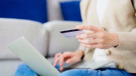 Young asian woman sitting on sofa in living room, makes online banking payments through the internet from bank card on computer laptop. Shopping online on notebook with credit cardの写真素材