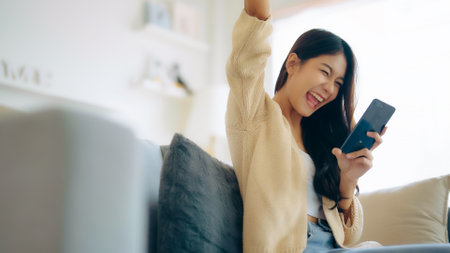 Happy young asian woman relax on comfortable couch at home texting messaging on smartphone, smiling girl use cellphone, chatting online message, shopping online from homeの写真素材