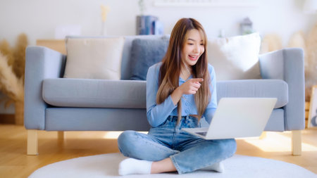 Young asian woman working on her laptop at home, grinning. attractive Asian woman utilizing computer for online schooling, video calling, and conference callsの写真素材