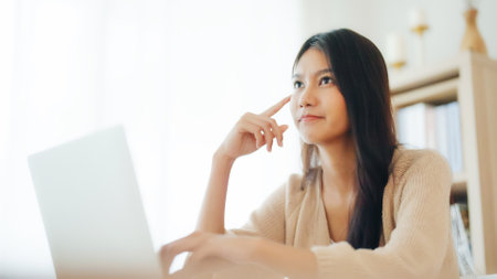 Young asian woman working on computer laptop on desk in living room at homeの写真素材
