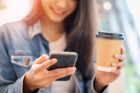 Young asian beautiful woman using smart phone in coffee shop cafe, typing write message on mobile, online shopping, transfer payment, internet bankingの写真素材