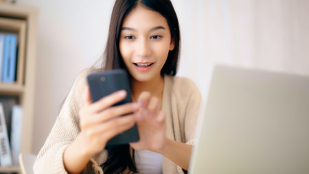 Young asian woman happy working on computer laptop and hand typing chat message on mobile smartphone at home. Video call, Online meetingの写真素材