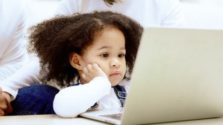 Happy african family parents and little children enjoy using computer laptop together sit on sofa, technology addicted couple with kids having fun at homeの写真素材