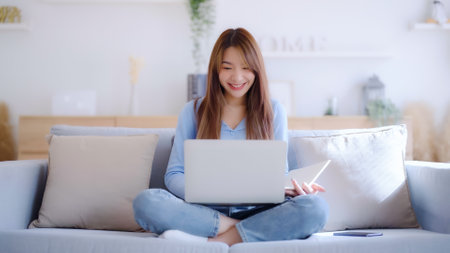 Young asian woman using laptop while seated on couch at homeの写真素材