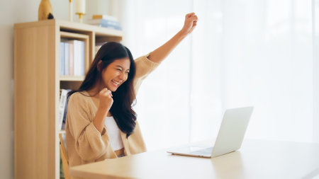 Funny euphoric young asian woman celebrating winning or getting ecommerce shopping offer on computer laptop. Excited happy girl winner looking at notebook celebrating successの写真素材