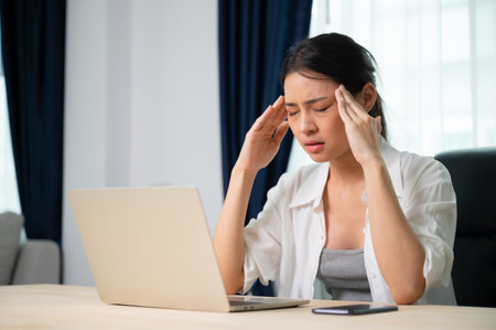 Office syndrome. Overworked tired young asian woman feeling headache, having eyesight problem after computer laptop work. Stressed young woman suffering from fatigue at homeの写真素材