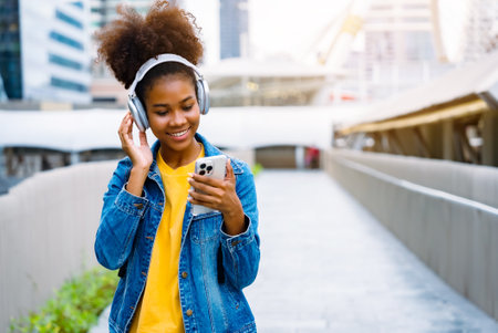 Cheerful black student girl wearing headset and using mobile smartphone, Walking at college building outdoor, Happy and smiling woman teenager. Modern educationの写真素材